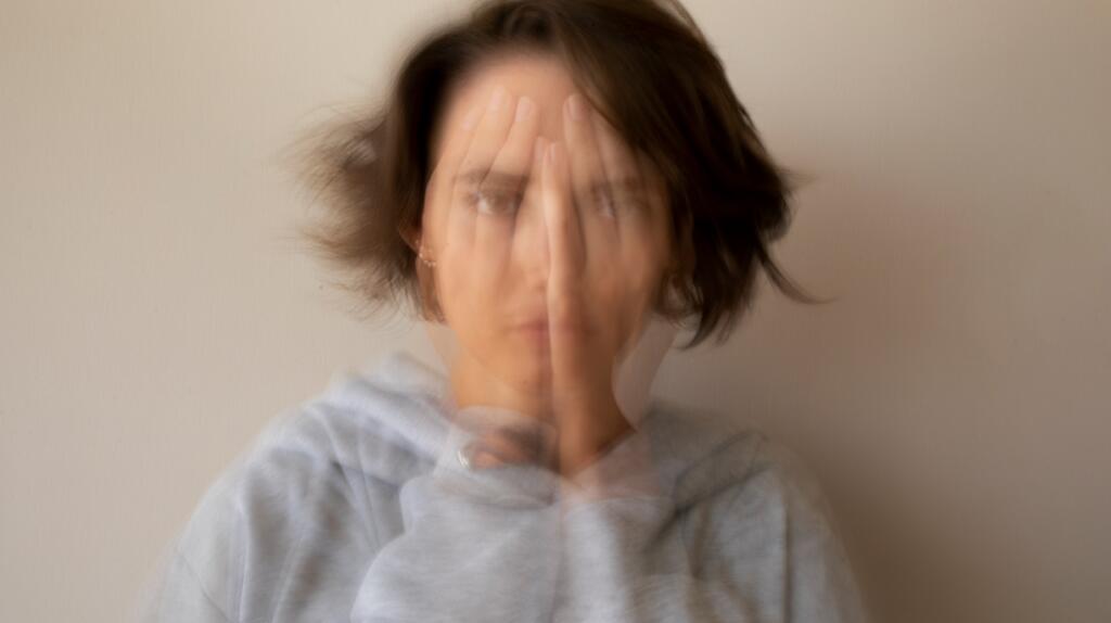 Vrouw met wazig bewegend gezicht, grijze trui, neutrale achtergrond.