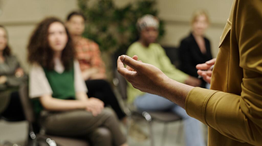 Een persoon spreekt voor een groep zittende mensen.