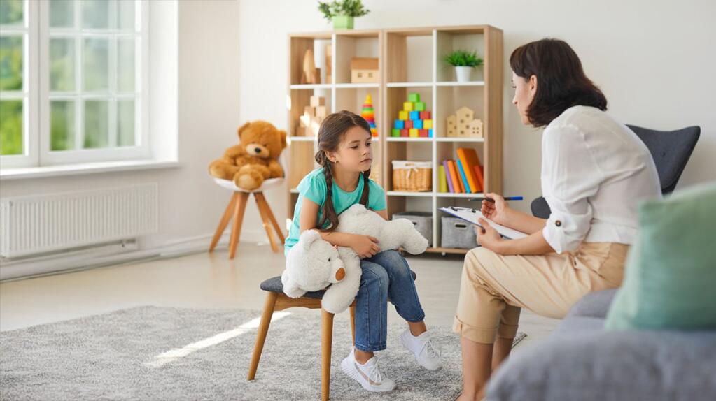 Meisje met knuffeldier praat met vrouw in een lichte kamer.