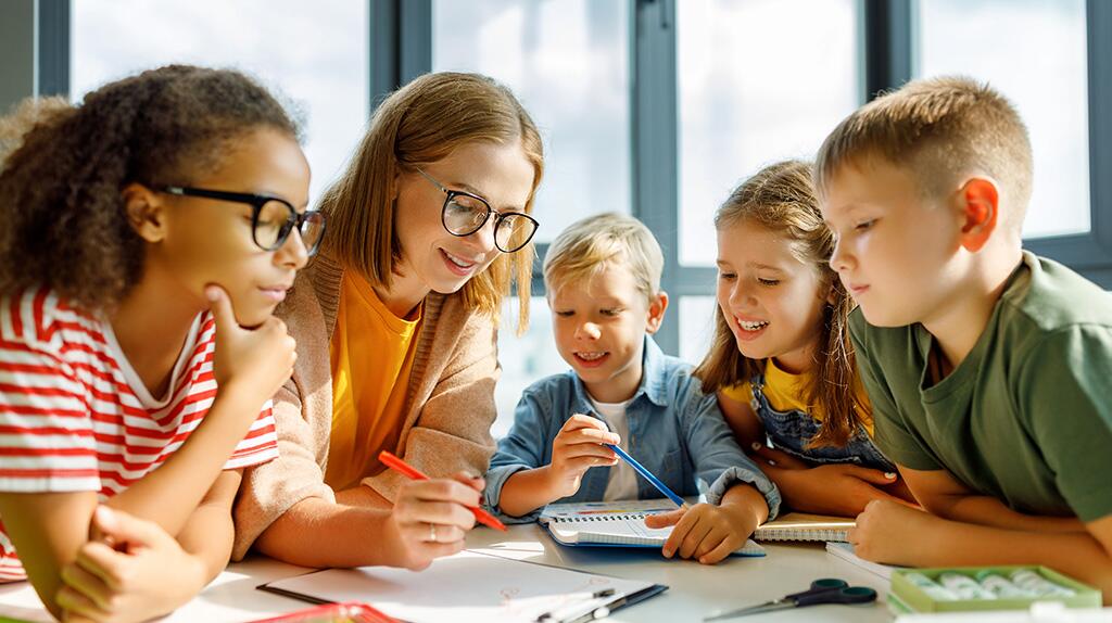 Kinderen en lerares werken samen aan een tafel, aandachtig en vrolijk.