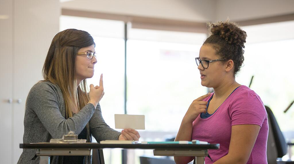 Twee vrouwen communiceren in gebarentaal in een moderne ruimte.