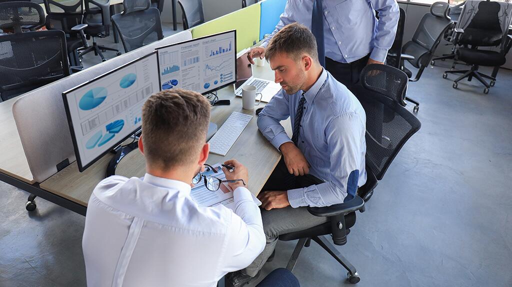 Twee mannen bekijken grafieken op computerschermen in een kantoor.