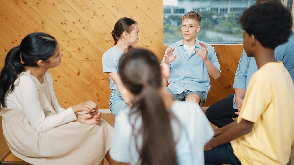 Groep mensen in gesprek, zittend in een kring in een warme, houten ruimte.