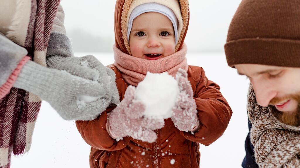 Kind speelt met sneeuwbal, winterkleding, lachend gezicht.