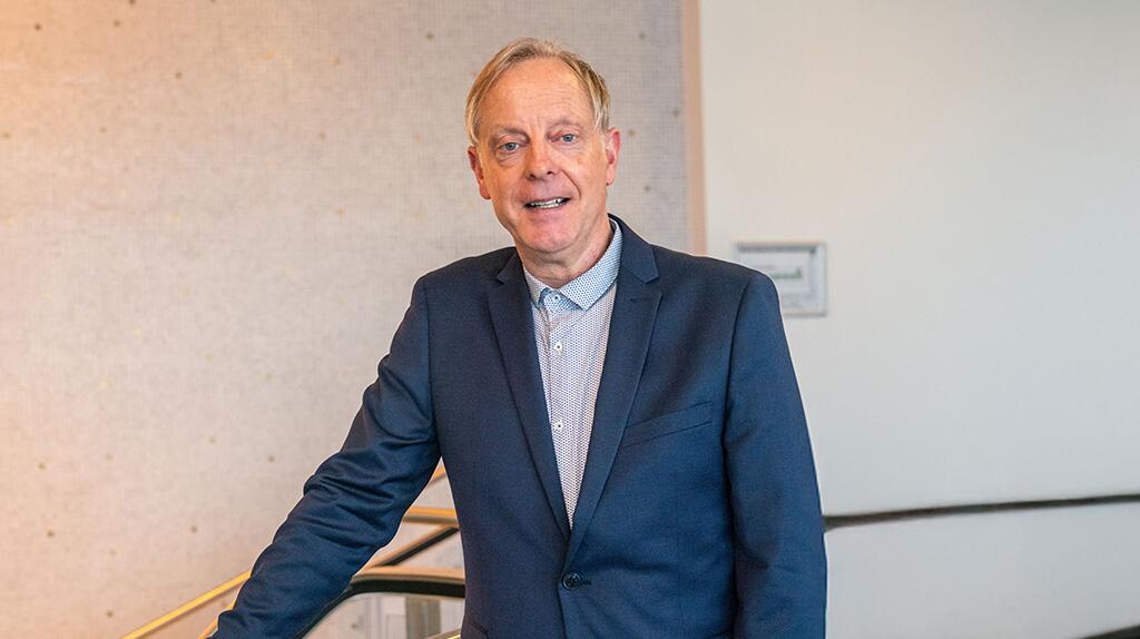 Man in pak lacht, staand in moderne ruimte.