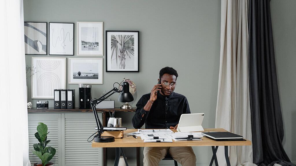 Man zit aan bureau met telefoon en laptop in moderne kantoorruimte.