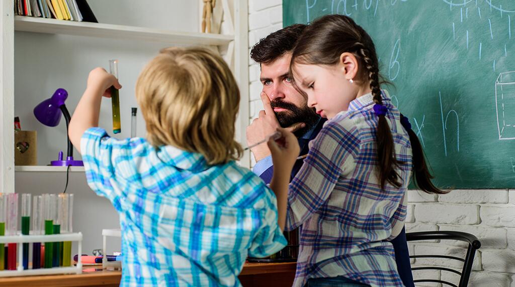 Twee kinderen experimenteren met buisjes in een klas met een leraar.