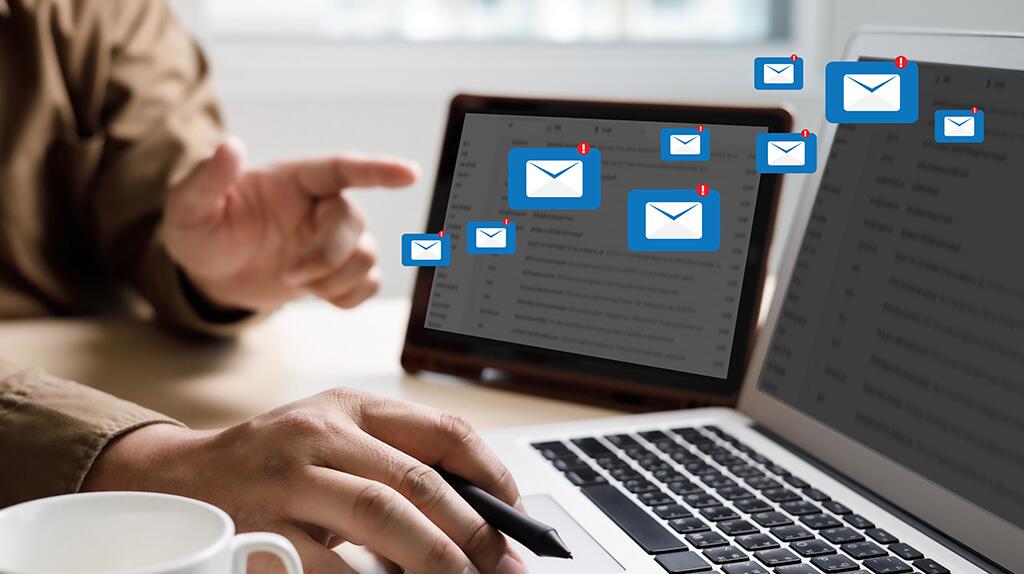 Laptop met open e-mails op scherm, handen tikken op toetsenbord.