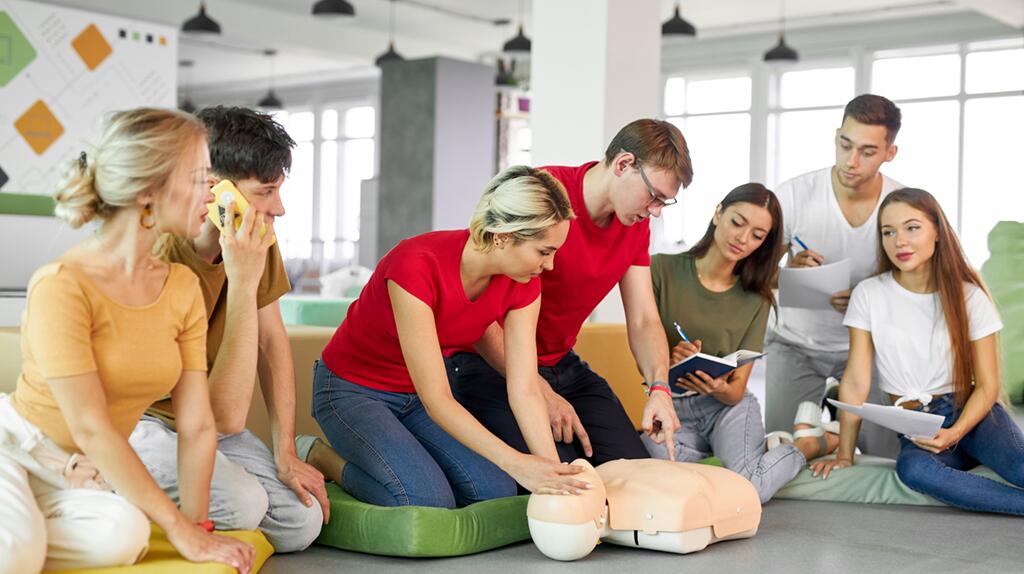 Groep mensen oefent reanimatie op een pop in een klaslokaal.