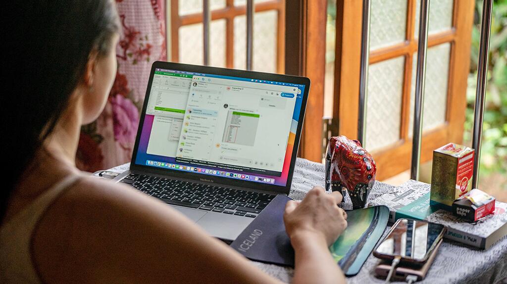 Persoon werkt op laptop met raam op achtergrond, zonnige dag.