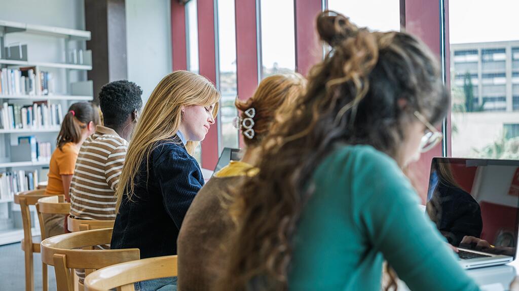 Mensen studeren in een bibliotheek aan houten tafels met laptops.
