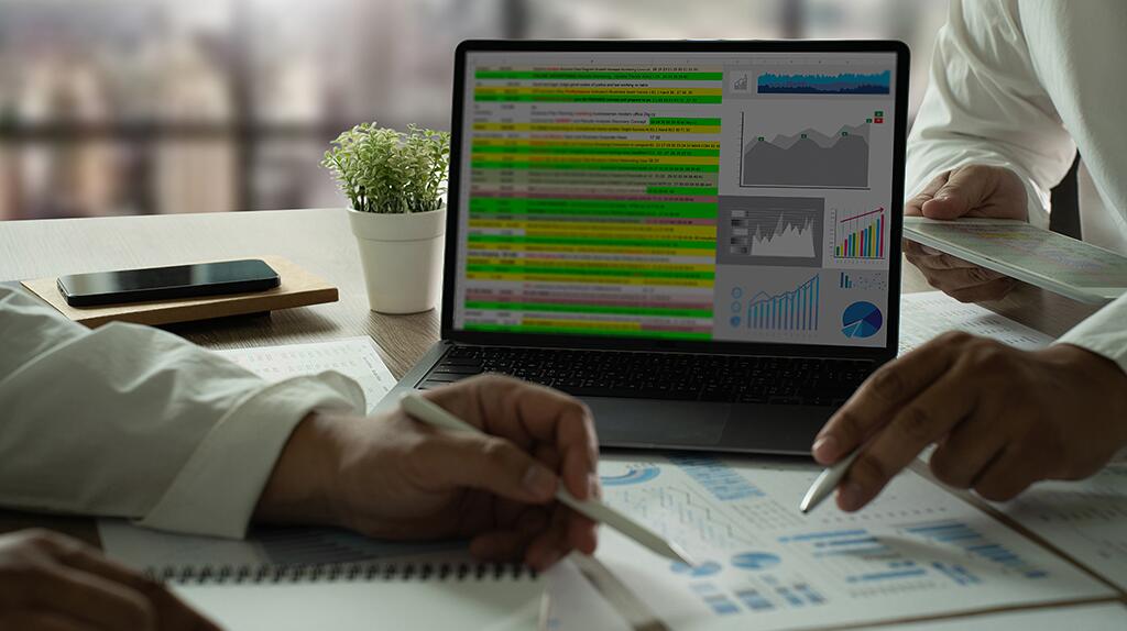 Laptop toont grafieken; mensen bespreken notities en documenten.
