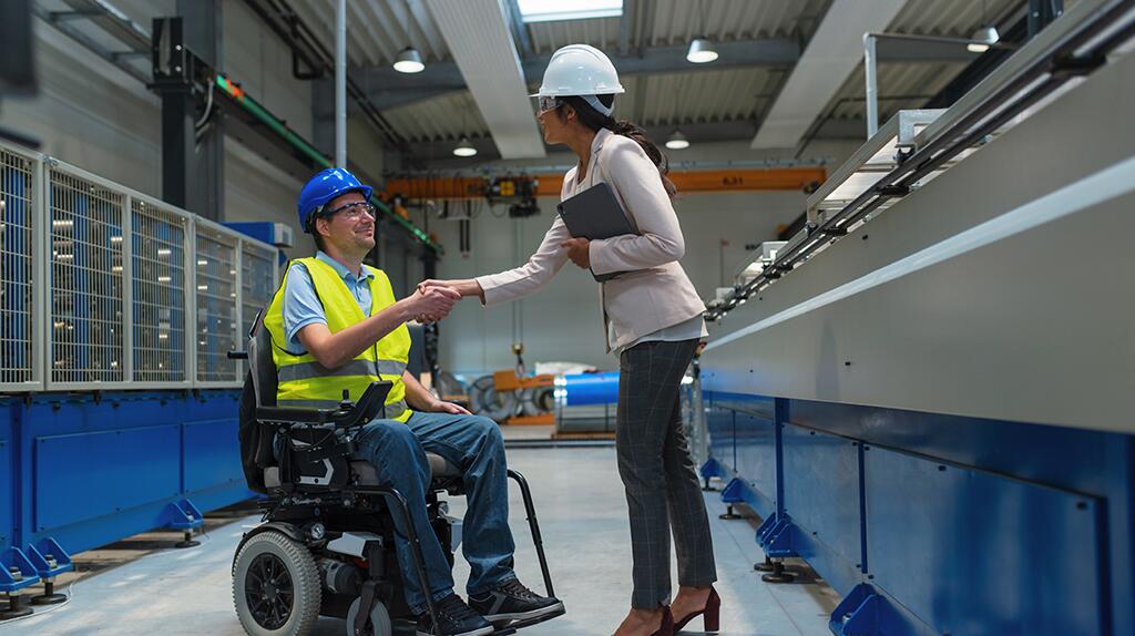Ingenieur en arbeider in rolstoel schudden handen in fabriekshal.