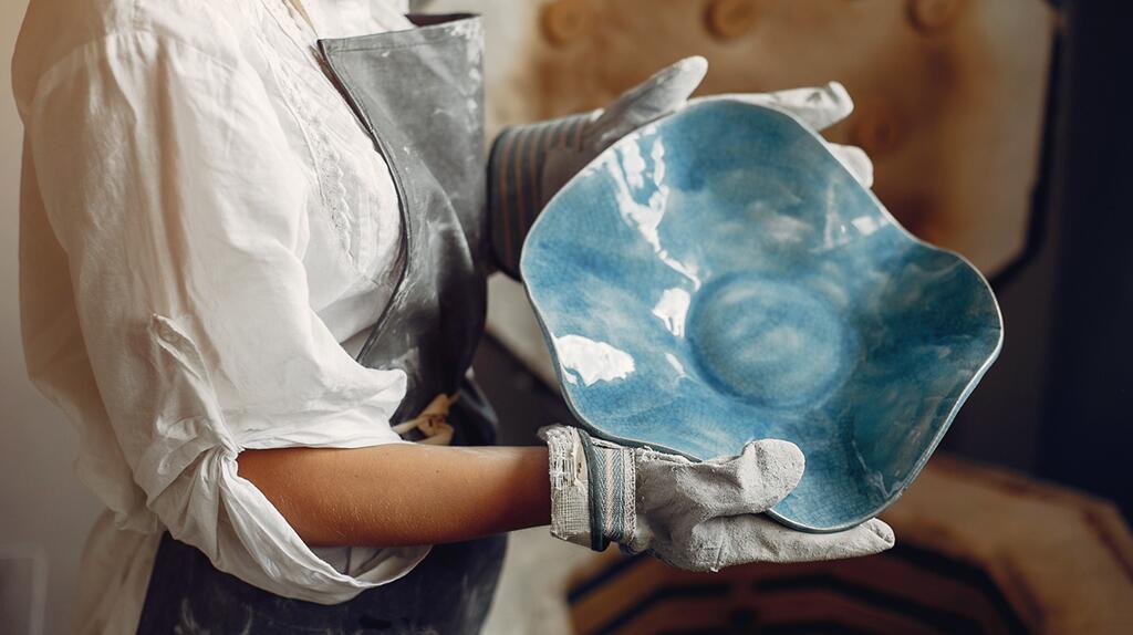 Persoon in schort houdt blauwe, keramische schaal vast.