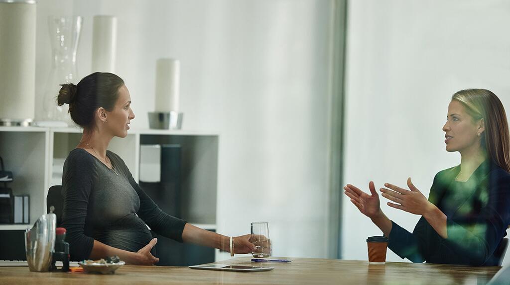 Twee vrouwen in gesprek aan tafel in een moderne kantoorruimte.