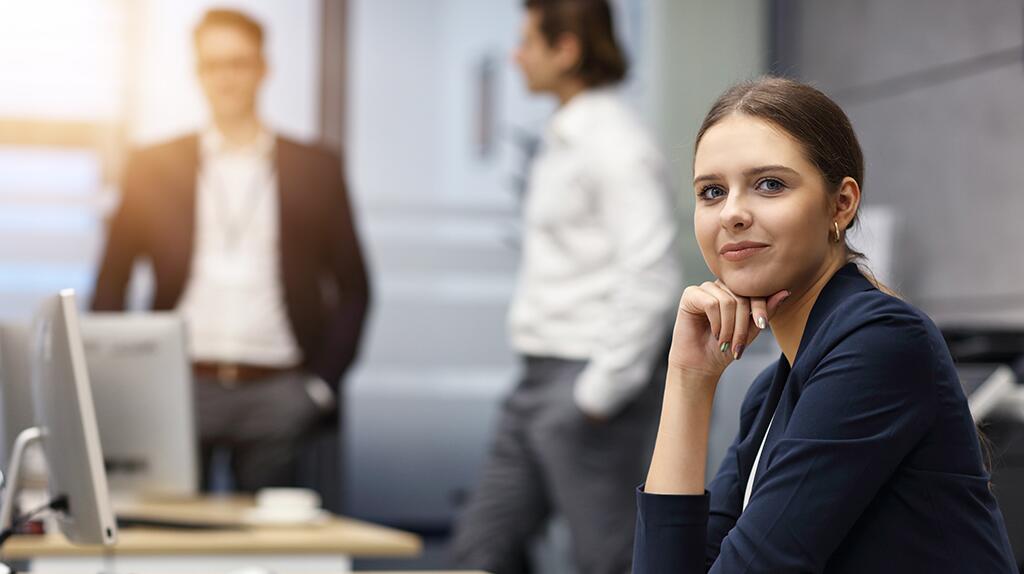 Vrouw in kantoor kijkt serieus, drie collega's op de achtergrond.