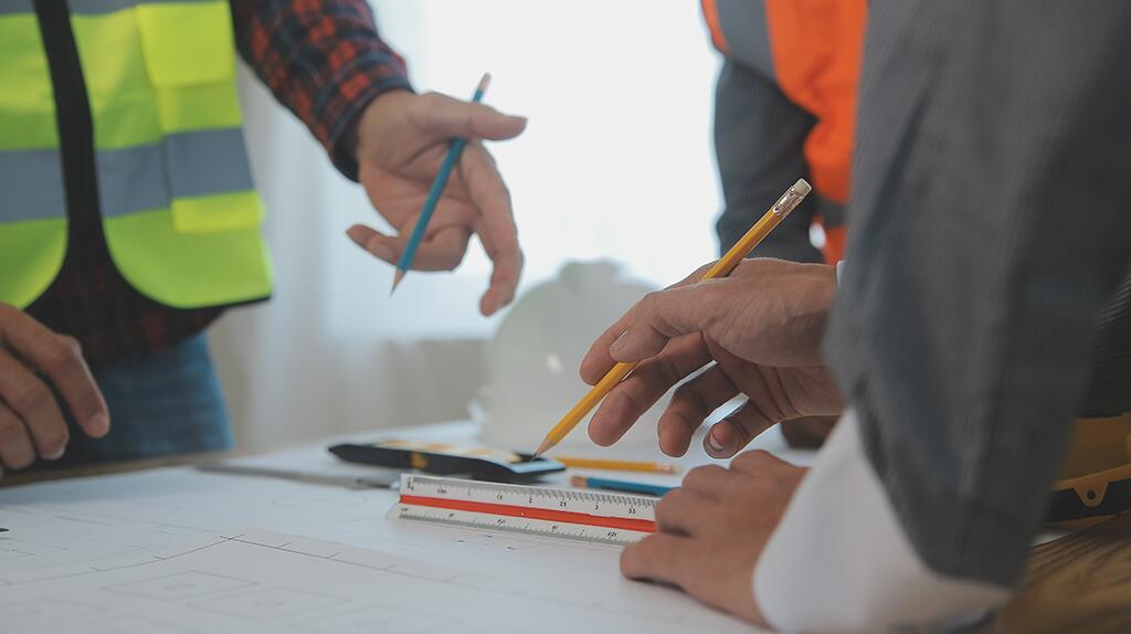 Mensen in reflecterende vesten bespreken plannen op een tafel.
