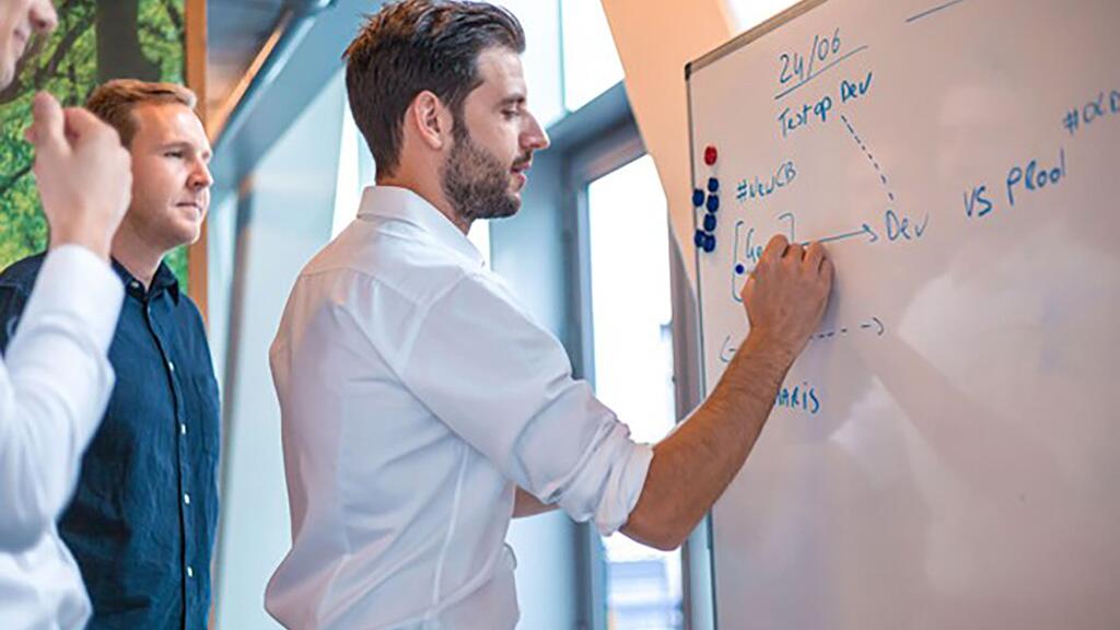 Drie mannen brainstormen bij een whiteboard in een kantooromgeving.