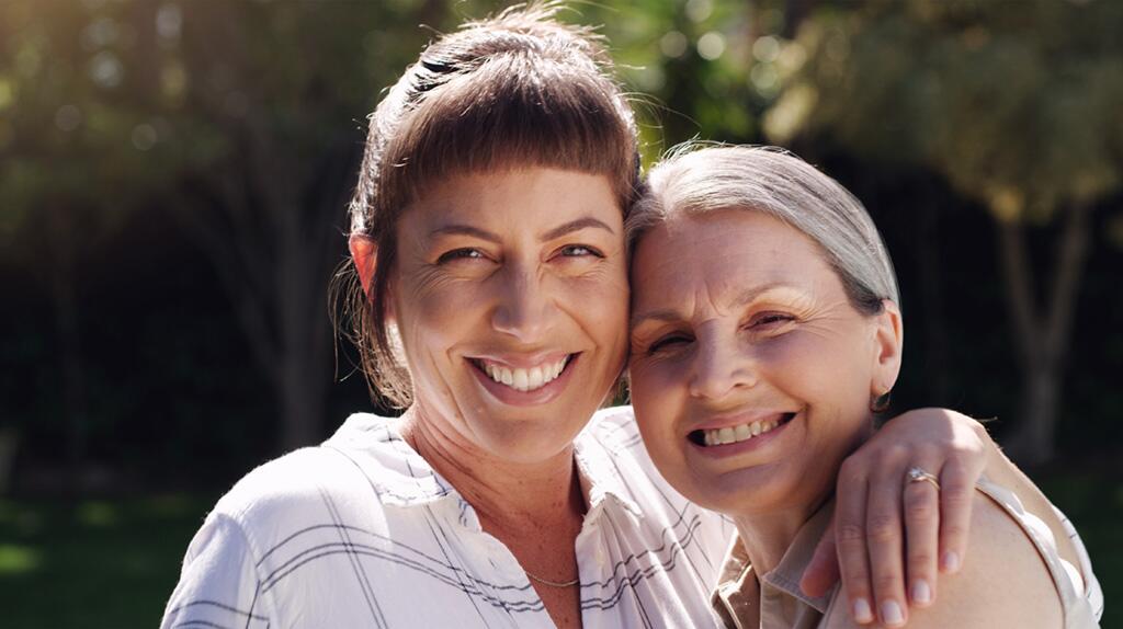 Twee lachende vrouwen omarmen elkaar buiten in de zon.