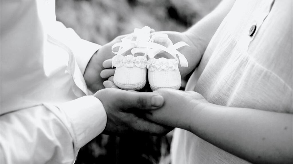 Handen houden kleine babyschoenen vast, zwart-wit foto.