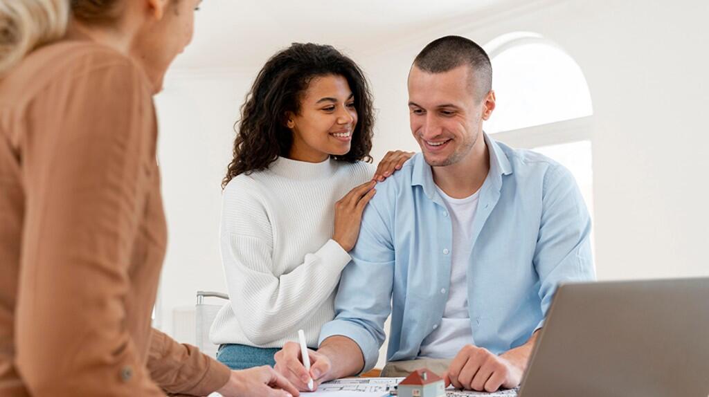 Drie mensen glimlachen terwijl ze samenwerken aan een bureau met laptop en papieren.