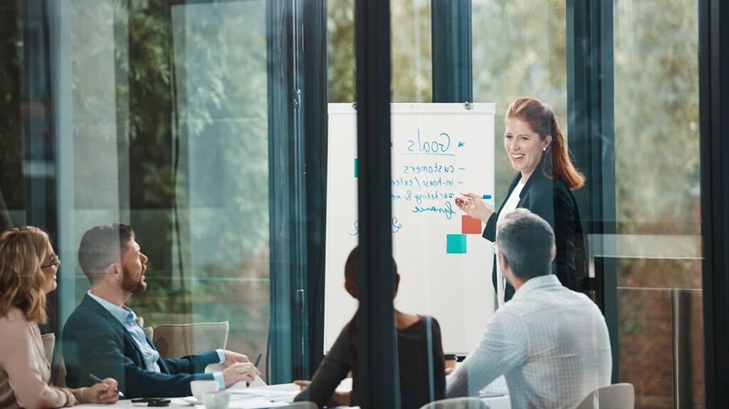 Een vrouw presenteert aan collega's in een vergaderruimte.