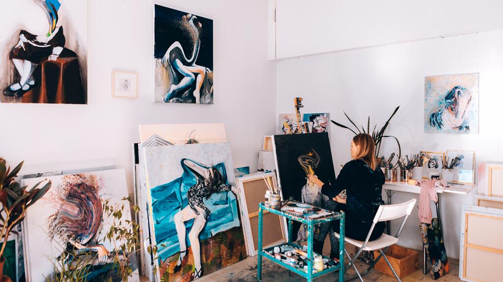 Kunstenaar schildert in studio omringd door kleurrijke kunstwerken.