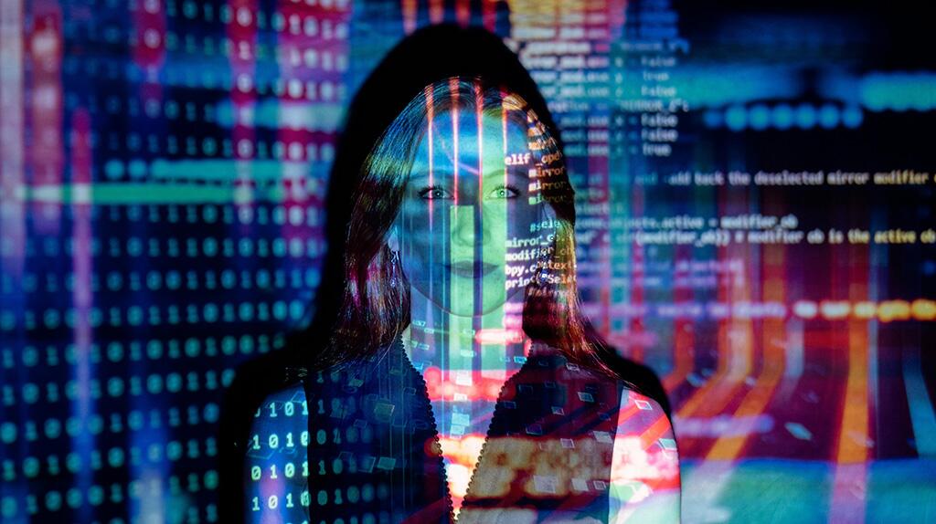 Persoon met bril kijkt naar code en gegevens op een scherm, met blauw en rood licht.