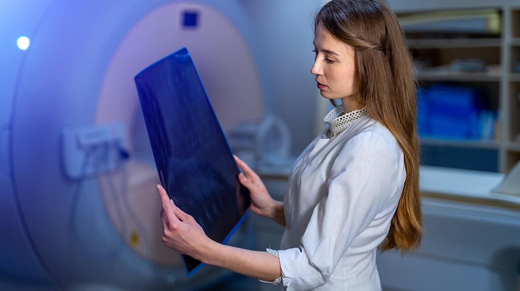 Vrouw bekijkt röntgenfoto bij MRI-scanner in helder verlichte kamer.