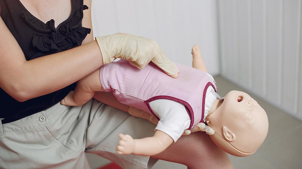 Persoon oefent EHBO op babypop met roze kleding.