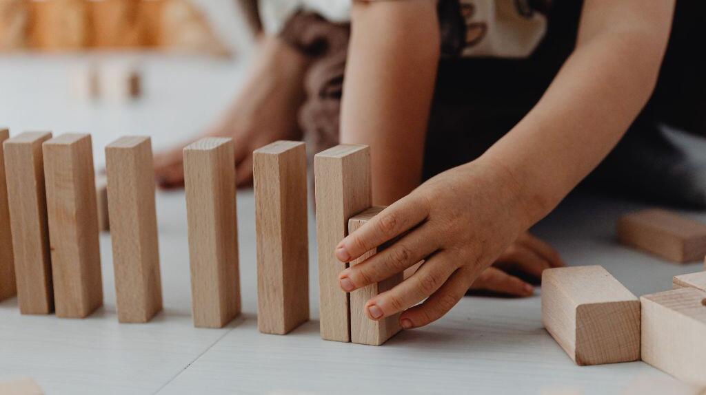 Twee handen stapelen houten blokken op een witte vloer.