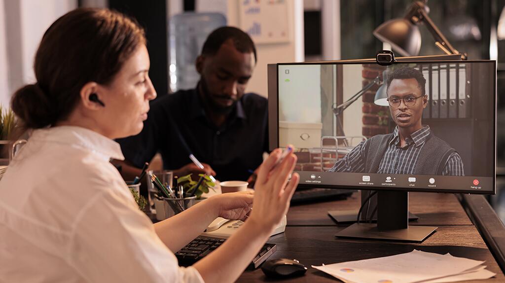 Vergadering via videoconferentie, vrouw communiceert met scherm in kantooromgeving.