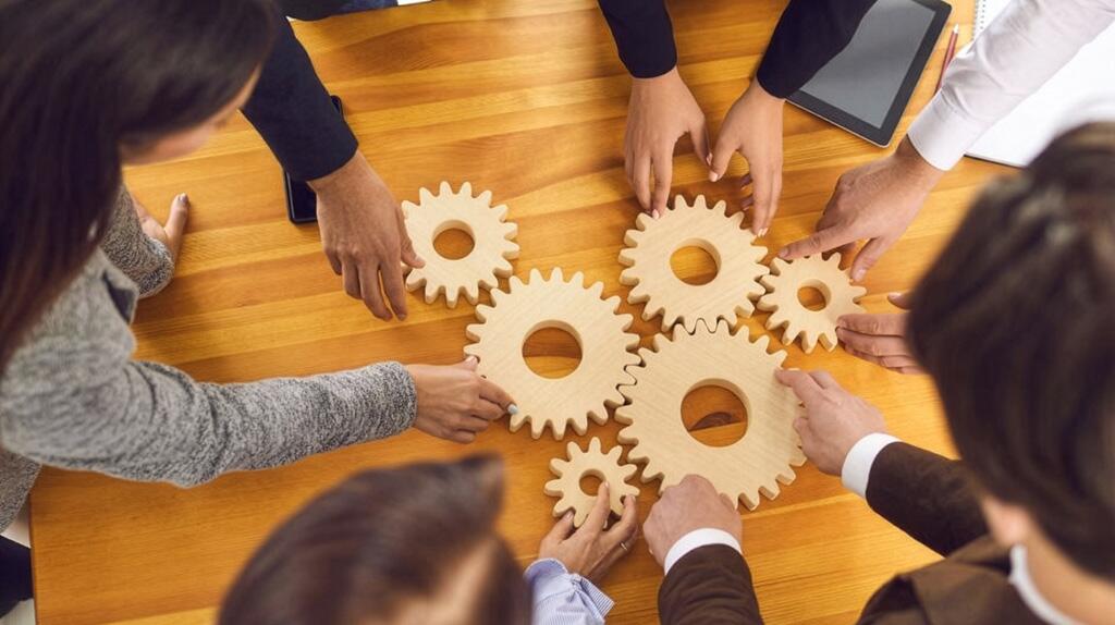 Handen leggen houten tandwielen op tafel, teamworkconcept.