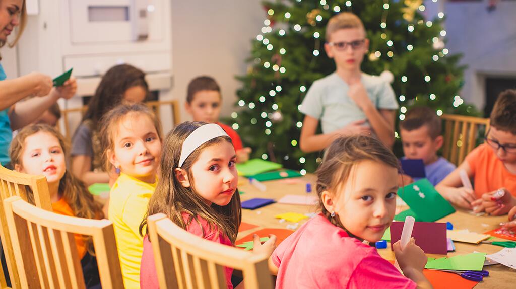 Kinderen knutselen rond een tafel, met kerstboom op achtergrond.