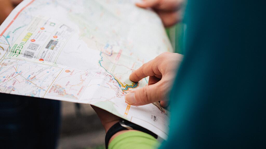 Twee handen houden een plattegrond vast en wijzen erop.