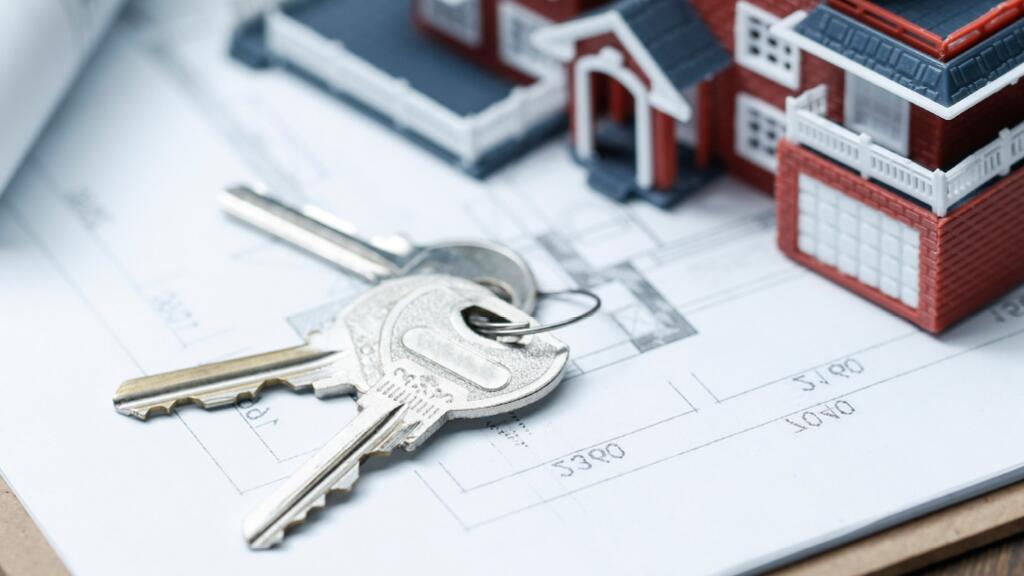 Sleutels op architectuurtekening bij miniatuurhuis.