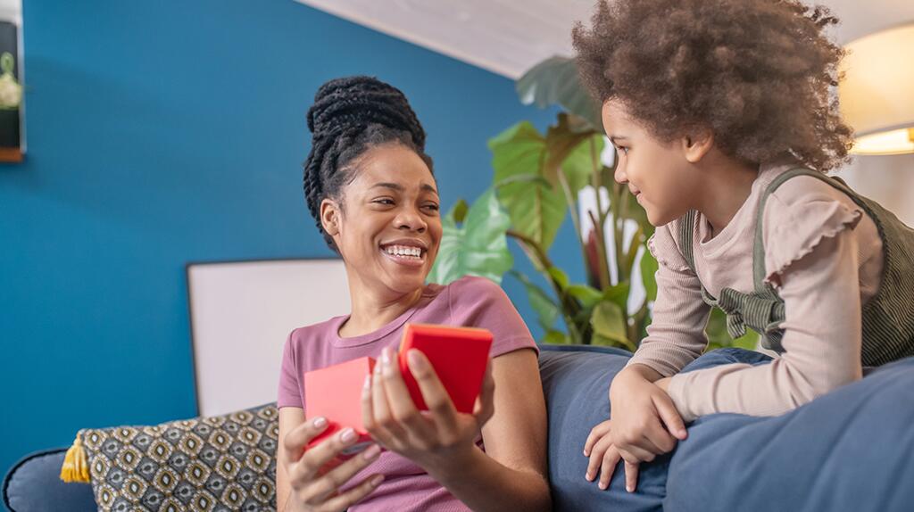 Vrouw en kind lachen op een bank met een rood cadeau in hun handen.