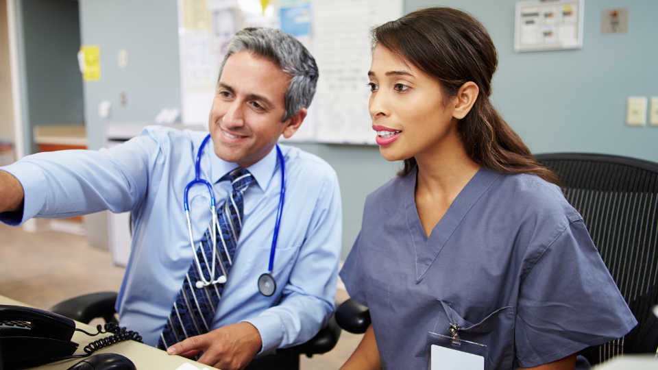 Dokter en verpleegkundige kijken naar computerscherm in ziekenhuisomgeving.