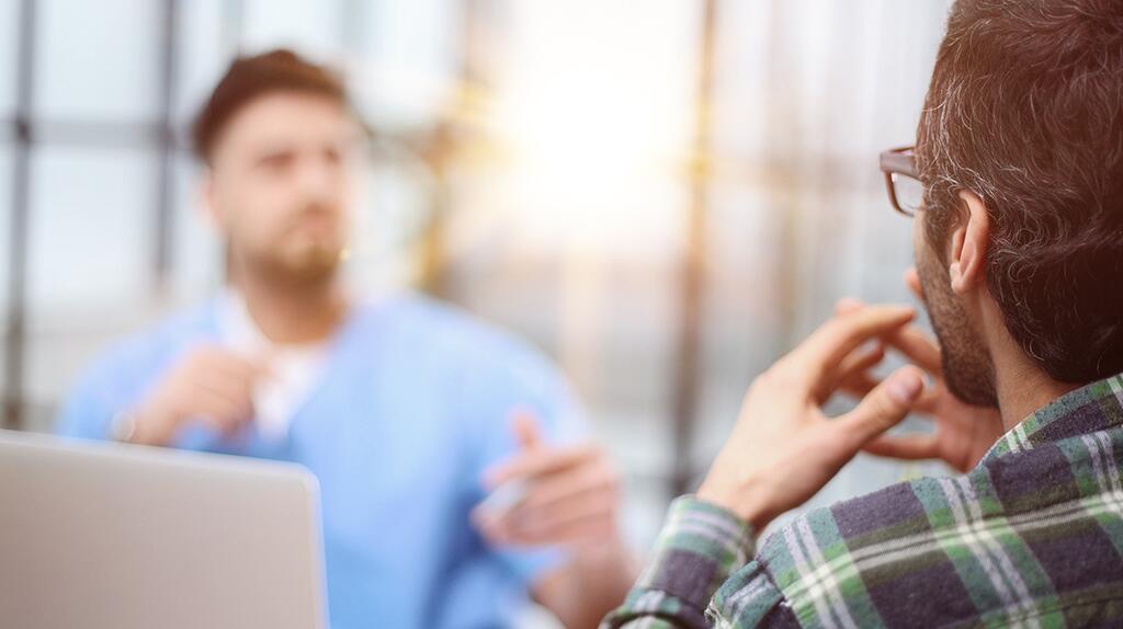 Twee mannen in gesprek, een draagt een blauwe trui, de ander een geruite blouse.