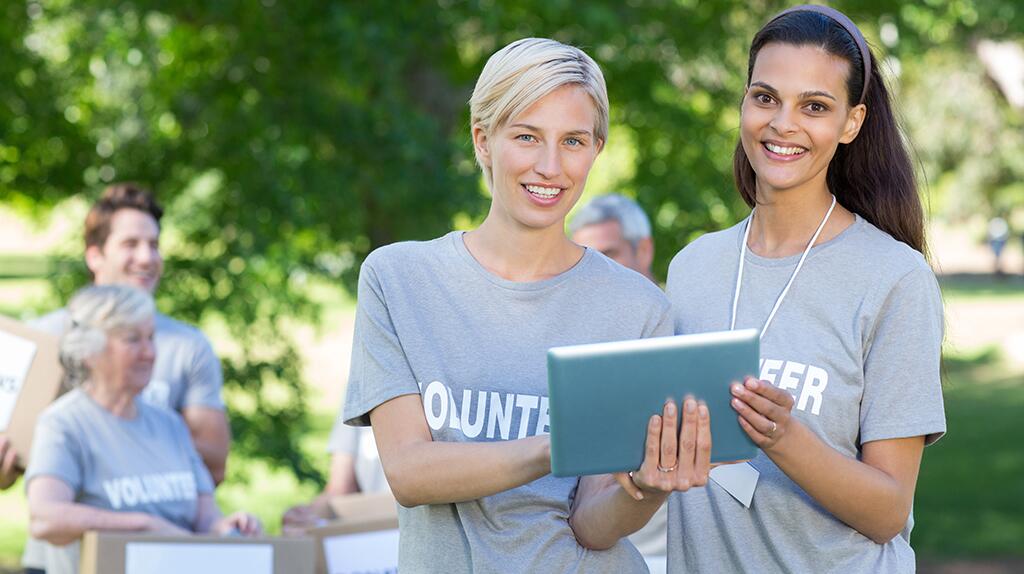 Twee lachende vrijwilligers met tablet in een park.