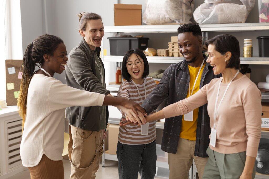Groepje lachende mensen met handen in het midden in een opslagruimte.