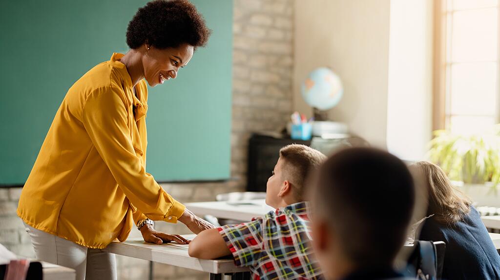 Leraar in gele blouse helpt leerling in klaslokaal.