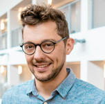 Man met bril en krullend haar glimlacht binnenshuis.