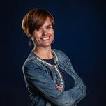 Vrouw glimlachend met armen gekruist, donkerblauwe achtergrond.