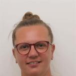 Persoon met bril en knot, glimlacht licht voor witte achtergrond.