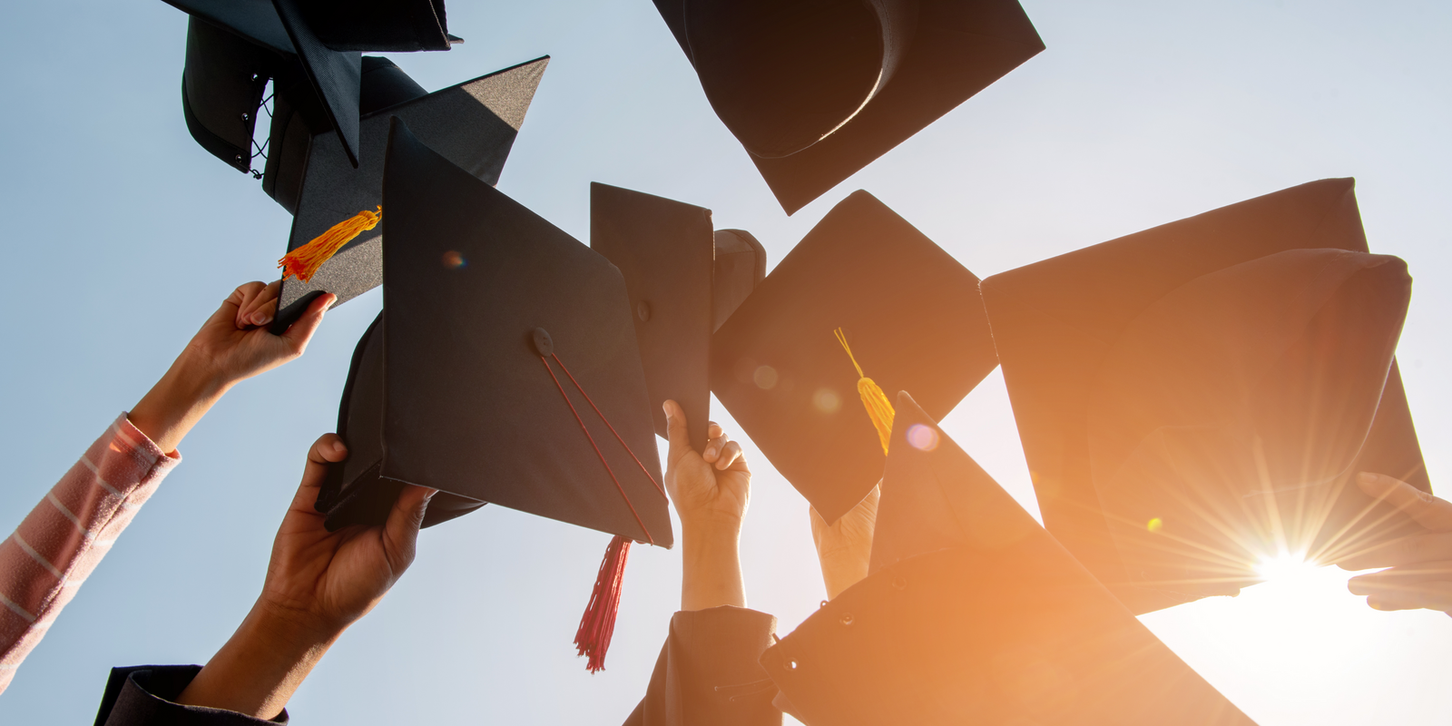 Afgestudeerden gooien hoedjes in de lucht tegen heldere lucht.