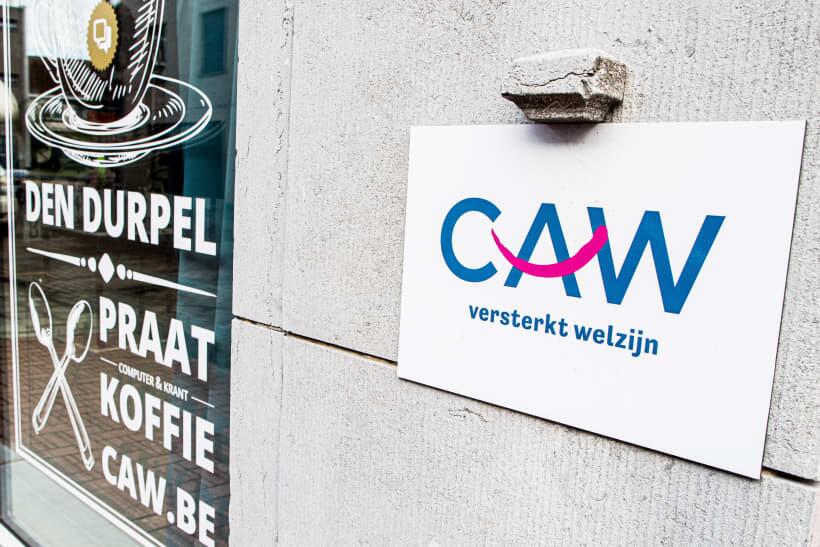 CAW-logo op een muur naast een caféraam met koffieposter.