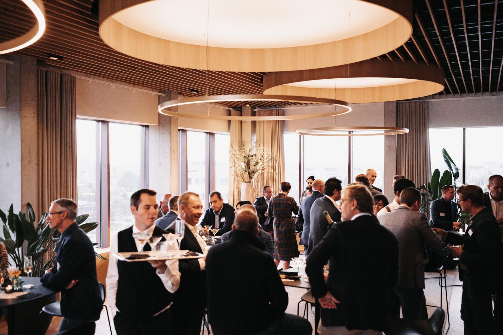 Zakelijke bijeenkomst, mannen in pakken praten in een moderne zaal met grote hanglampen.