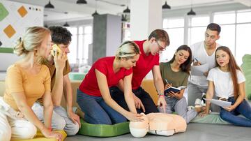 Groep mensen oefent reanimatie op een pop in een klaslokaal.