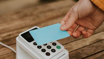 Hand houdt een blauwe kaart boven een witte betaalterminal.